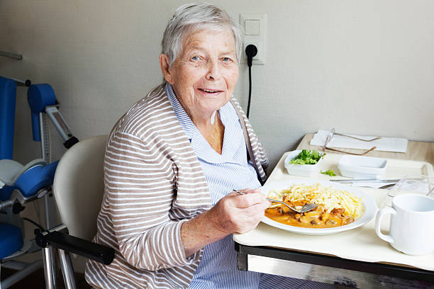senior female patient, eating food from tray in hospital